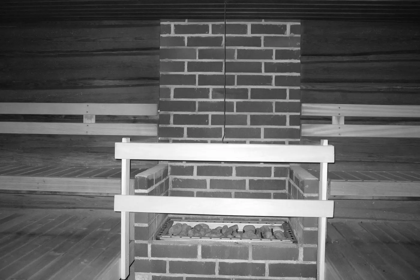 A brick sauna heater topped with a bed of stones, set into a timber-lined room with slatted benches on either side.