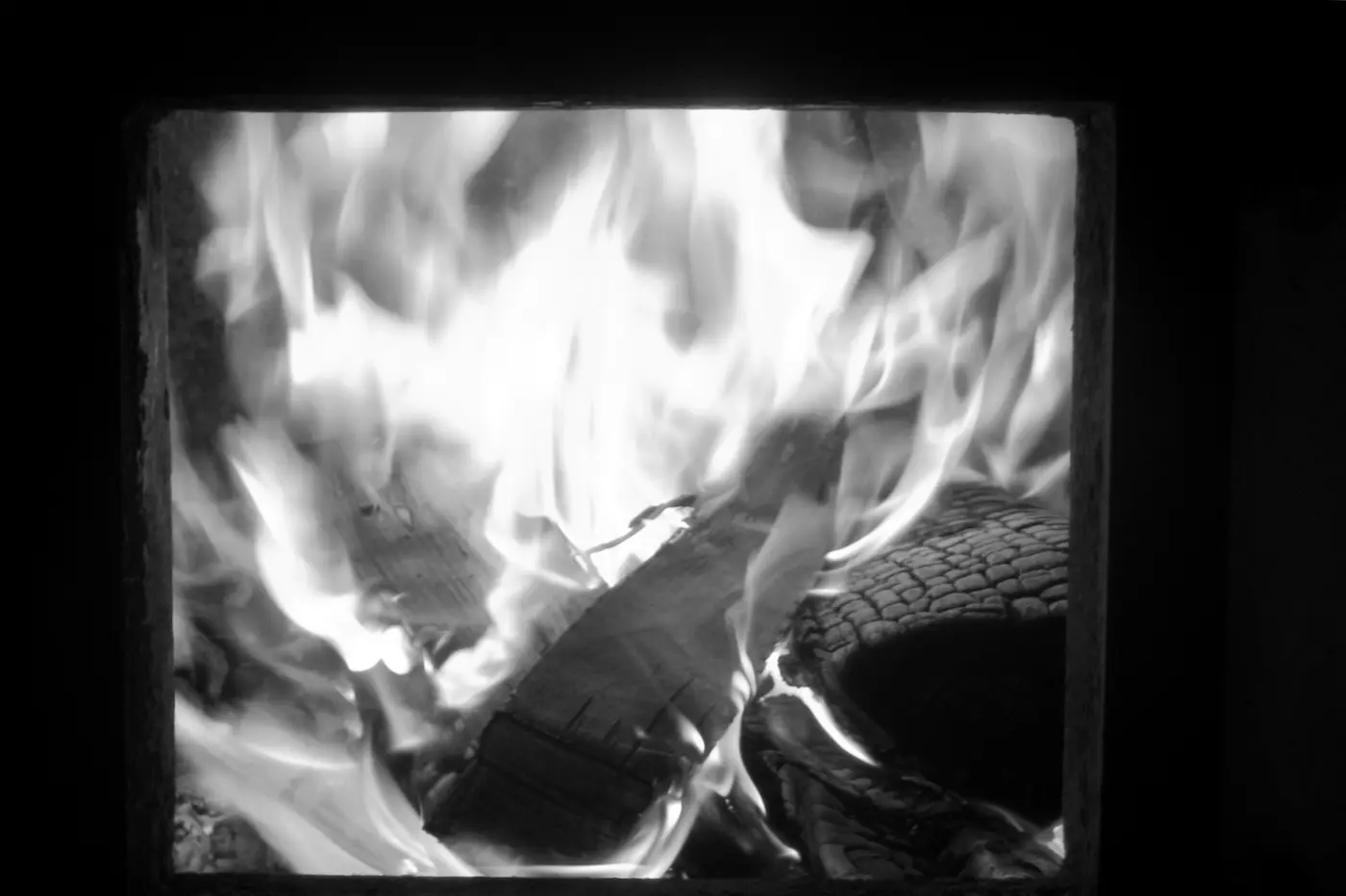 Flames and charred logs seen through the open door of a wood-burning sauna stove.